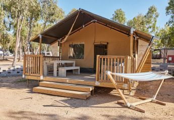 Tenda safari con veranda in legno, tavolo da picnic e amaca presso Villatent Outback, tra gli alberi.