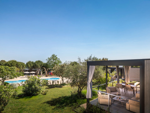 Overdekt terras van Premium Holiday Home met loungeset en uitzicht op zwembad in groene omgeving.