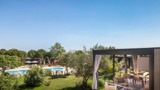 Overdekt terras van Premium Holiday Home met loungeset en uitzicht op zwembad in groene omgeving.