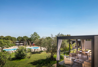 Vista dalla veranda arredata della Premium Holiday Home su giardino curato e piscina immersi nel verde.