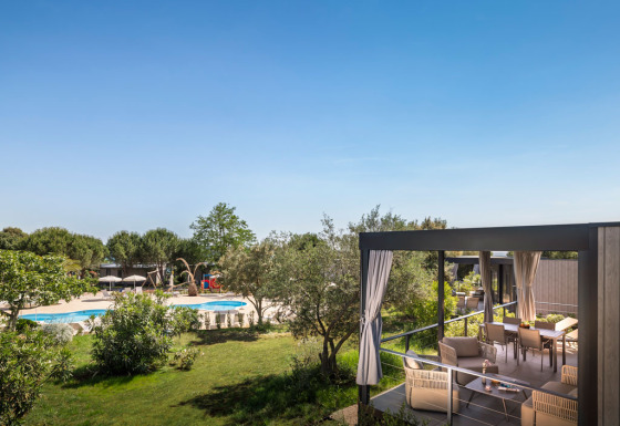 Overdekt terras van Premium Holiday Home met loungeset en uitzicht op zwembad in groene omgeving.