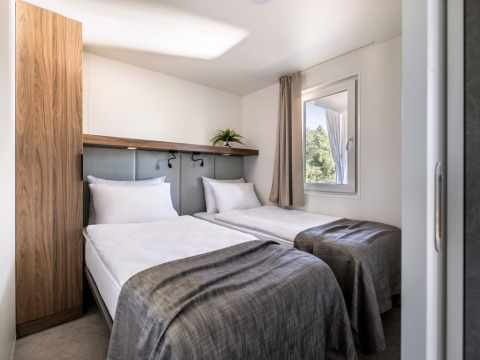 Slaapkamer met twee eenpersoonsbedden, moderne inrichting en raam in Premium Holiday Home bij Camping Sirena, Kroatië.