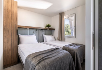 Slaapkamer met twee eenpersoonsbedden, moderne inrichting en raam in Premium Holiday Home bij Camping Sirena, Kroatië.