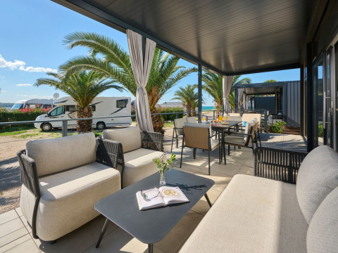 Luxe vakantiewoning met overdekt terras en moderne meubels bij palmbomen op Aminess Planet Camping Sirena, Kroatië.