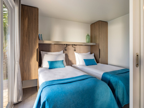Twee eenpersoonsbedden met turquoise beddengoed in een moderne cabin op Aminess Planet Camping Sirena, Kroatië.