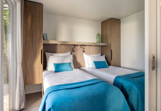 Twee eenpersoonsbedden met turquoise beddengoed in een moderne cabin op Aminess Planet Camping Sirena, Kroatië.