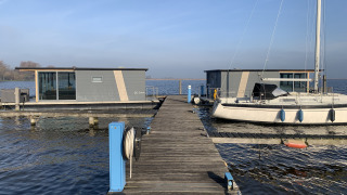 Foto van Houseboat «Havenlodge» bij Marina Uitgeest in Nederland, met afgemeerde boten en houten steiger.