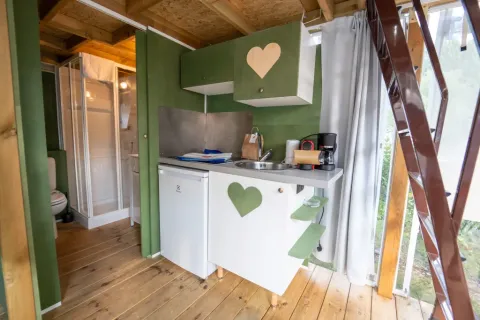 Compact kitchen and bathroom inside Airlodge 1 at Chianti Glamping Resort, Italy, with green cabinets and wood.