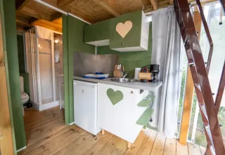 Compact kitchen and bathroom inside Airlodge 1 at Chianti Glamping Resort, Italy, with green cabinets and wood.