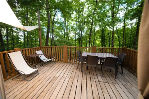 Wooden deck with lounge chairs and dining table surrounded by lush forest at Airlodge 1, Chianti Glamping Resort.