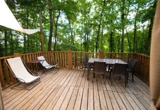 Wooden deck with lounge chairs and dining table surrounded by lush forest at Airlodge 1, Chianti Glamping Resort.
