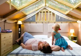 A woman and a child relax on a bed under a glass roof in Airlodge 1 at Chianti Glamping Resort, Italy.