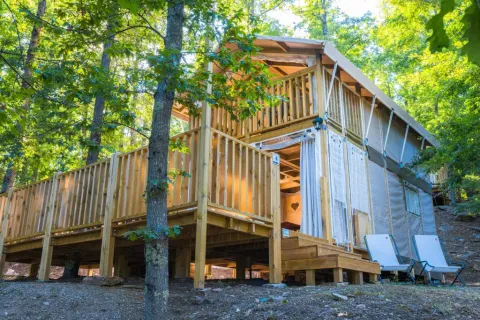 Buitenaanzicht van Airlodge 2.0, een knusse houten lodge met terras gelegen tussen de bomen van een bos.