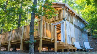 Buitenaanzicht van Airlodge 2.0, een gezellige houten lodge met balkon te midden van groene bosrijke natuur.