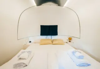Gezellige slaapkamer in de Airstream tiny house bij Chianti Glamping Resort, Italië, met frisse witte lakens.