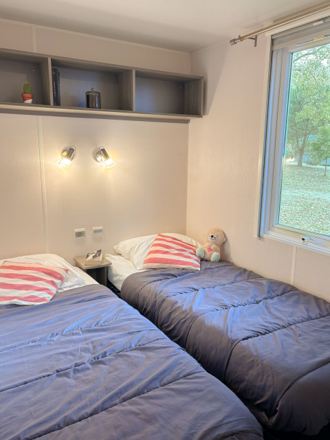 En hyggelig kabine med to enkelt senge, bløde grå dyner og et vindue med udsigt til grøn natur.