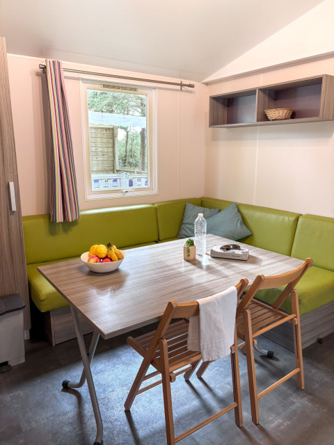 Coin repas du Mobile Home Comfort, Campsite Demoiselles Plage en France avec bol de fruits et meubles bois.