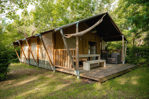 Safari-Zelt Villatent Nomad mit Holzterrasse auf Camping La Chiocciola in Italien, umgeben von Bäumen.