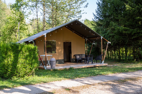 Safari tent on a green, wooded campsite with outdoor terrace seating, perfect for glamping stays.