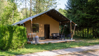 Safari-Zelt auf einem grünen, bewaldeten Campingplatz mit Terrasse und Gartenmöbeln im Freien.