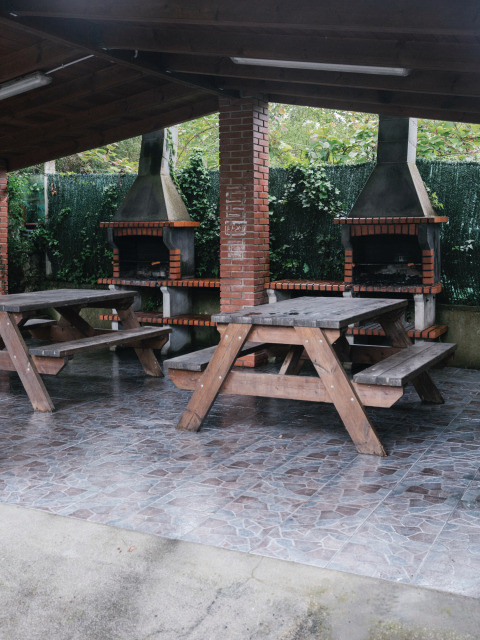 Überdachter Grillbereich mit Holzbänken und gemauerten Grills im Ferienpark Wecamp Cudillero, Asturien.