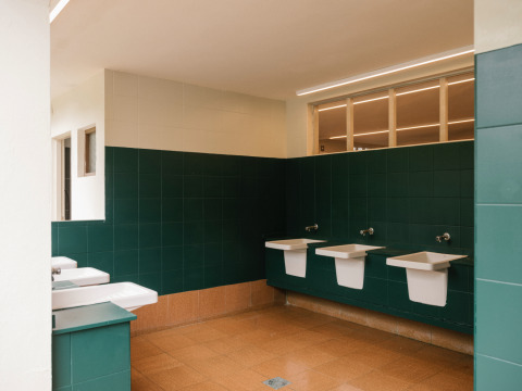 Modernes Badezimmer mit grünen Fliesen, weißen Waschbecken und braunen Böden im Wecamp Cudillero, Asturien, Spanien.