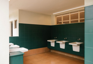 Modernes Badezimmer mit grünen Fliesen, weißen Waschbecken und braunen Böden im Wecamp Cudillero, Asturien, Spanien.