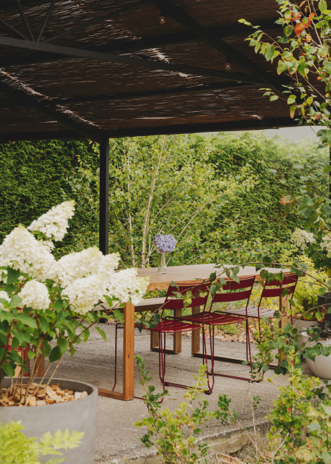 Überdachte Gartenterrasse im Wecamp Cudillero, Asturias, Spanien, mit Holztisch, roten Stühlen und Blumen.