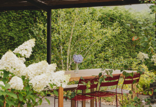 Überdachte Gartenterrasse im Wecamp Cudillero, Asturias, Spanien, mit Holztisch, roten Stühlen und Blumen.