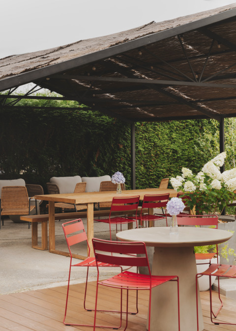 Überdachter Terrassenbereich im Wecamp Cudillero, Spanien, mit roten Stühlen und Blumendeko.