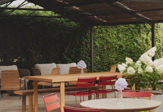 Überdachter Terrassenbereich im Wecamp Cudillero, Spanien, mit roten Stühlen und Blumendeko.