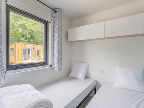 Modern twin room in a cottage at Campsite Seasonova du Chêne, France, with window view of another wooden lodge.