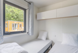 Modern twin room in a cottage at Campsite Seasonova du Chêne, France, with window view of another wooden lodge.