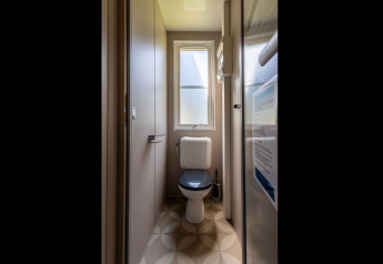 Baño estrecho con inodoro y ventana, visto en la Lodge «XL - comfort» del Holiday Park Bergumermeer en los Países Bajos.
