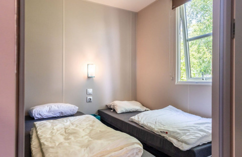 Room with two single beds, an open window and light walls in Lodge XL - comfort at Holiday Park Bergumermeer.