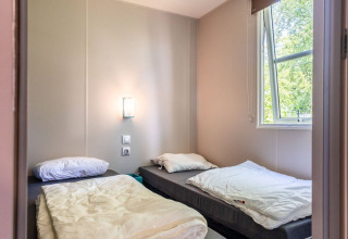 Room with two single beds, an open window and light walls in Lodge XL - comfort at Holiday Park Bergumermeer.