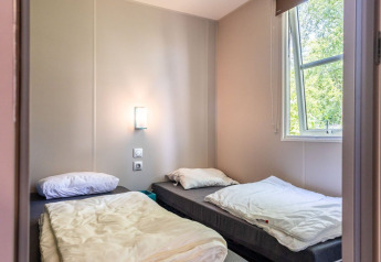 Chambre avec deux lits simples, fenêtre ouverte et murs clairs dans Lodge XL - comfort au Holiday Park Bergumermeer.
