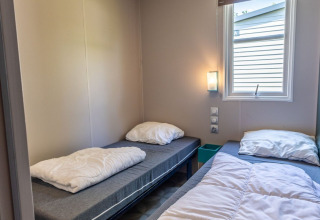Modern room with two single beds, window, and wall lamp in Lodge «XL - comfort» in the Netherlands.
