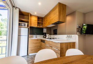 Modern kitchen setup with wooden furniture, appliances and dining area in Lodge «XL - comfort» at Holiday Park Bergumermeer.