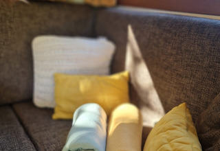 Canapé brun avec coussins et couvertures blancs et jaunes dans la tiny house 'Hans en Grietje' aux Pays-Bas.