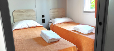 Zwei Einzelbetten mit orangefarbener Bettwäsche und weißen Handtüchern in der Mobile Home Riviera, San Marino.