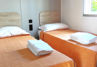 To enkeltsenge i en mobilhome hytte med orange sengetæpper og hvide håndklæder på Centro Vacanze San Marino.
