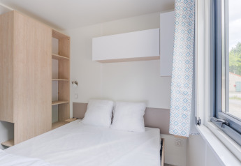 Stanza di lodge luminosa e moderna con letto matrimoniale, finestra aperta, scaffale e tendaggio blu.