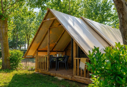 Safari Glamp Tent 2.0 met overdekte veranda, tafel en stoelen in een groen bosrijk kampeergebied.