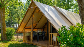 Safari Glamp Tent 2.0 with a covered porch, table and chairs, set in a green forest camping environment.