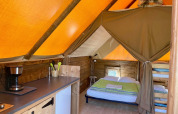 Interior of safari tent Glamp tent «2.0» at Weekend Glamping Resort, Italy, featuring beds and kitchenette.