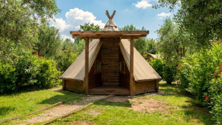 Tipi Junior Zelt umgeben von Bäumen und grünem Gras unter blauem Himmel, perfekt für naturnahes Camping.