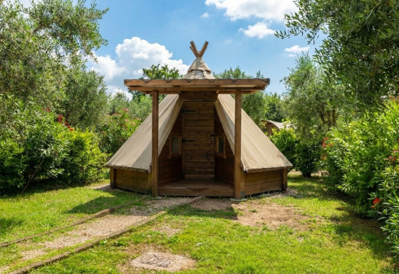 Tipi Junior tent omgeven door groen en bomen onder een blauwe lucht, ideaal voor een unieke kampeerervaring.