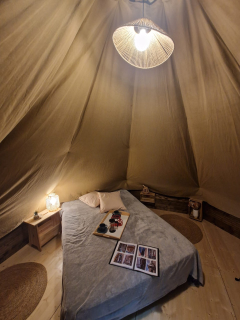 Knus interieur van een tipi tent met bed en zachte verlichting bij Tipi Junior, Weekend Glamping Resort, Italië.