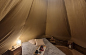 Interior acogedor de una tienda tipi con cama y luz suave en Tipi Junior, Weekend Glamping Resort, Italia.